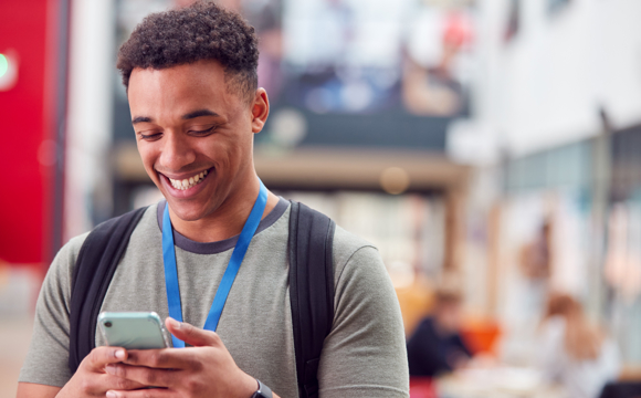 A smiling student using his phone to access his financial accounts.