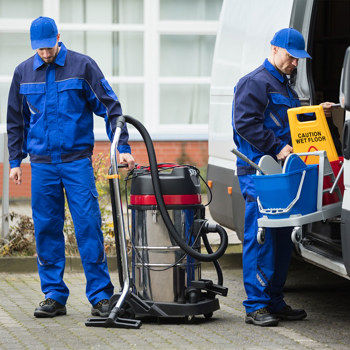 Two industrial cleaners in blue uniforms unloading equipment from a van