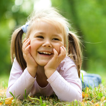 Little girl smiling in front of trees.