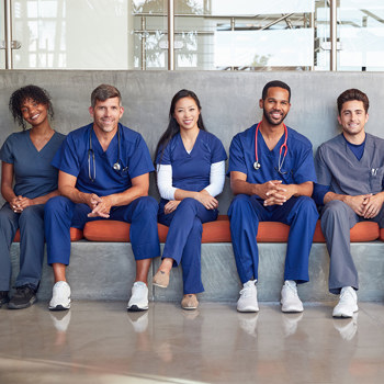 A row of medical professionals in scrubs sitting on a bench.