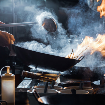 A steaming wok being stirred with flames underneath.
