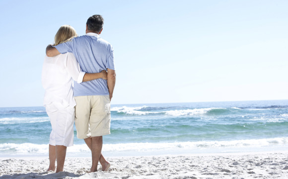 An older couple on the beach staring out at the water