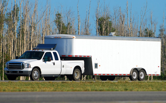 A long utility trailer being pulled by a white pickup.