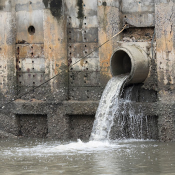 A large pipe dumping runoff water into a muddy body of water
