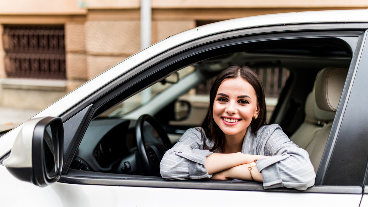 A young woman smiling out of the window of her car.