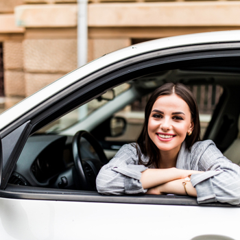 A young car owner smiling out the window of her sedan.