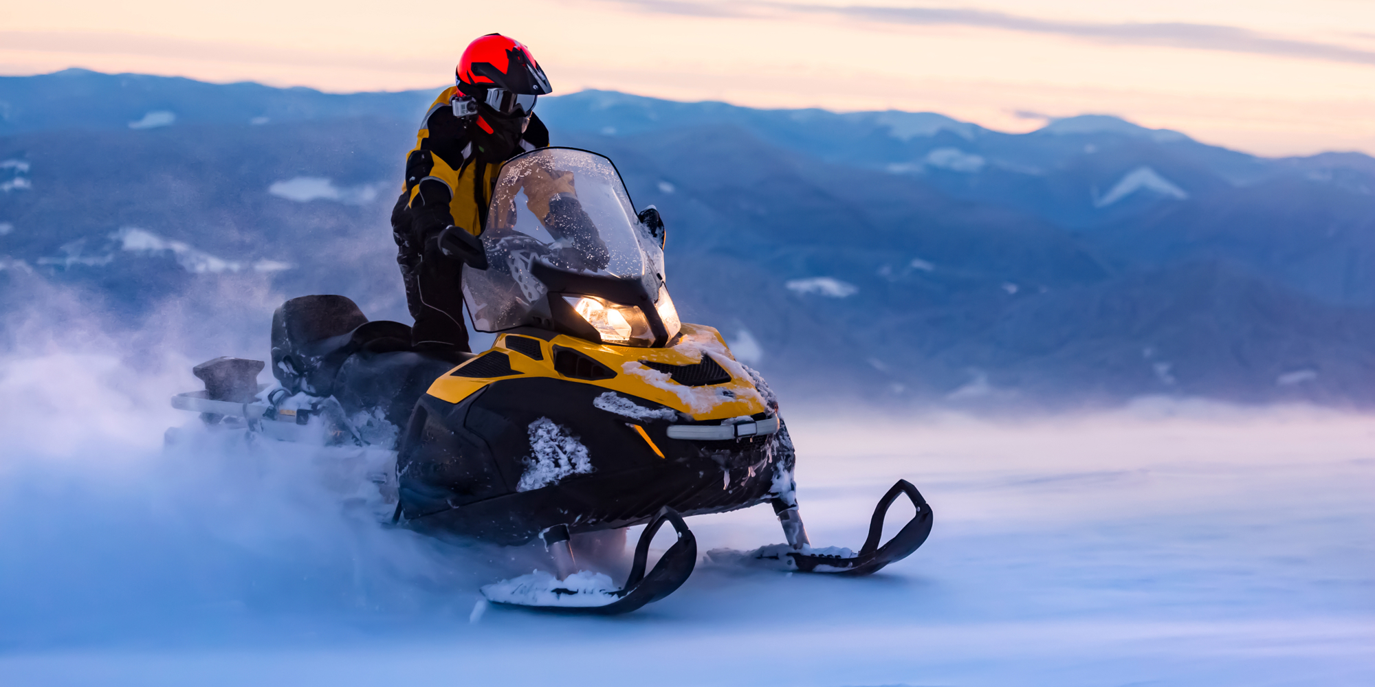 A snowmobile in the mountains with the sun setting.