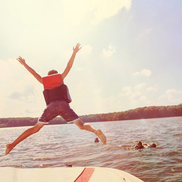 A kid jumping off a boat while others play in the water