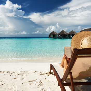 Woman in straw hat sitting on a beach chair by the ocean.