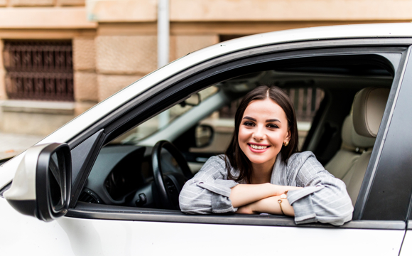 A woman smiling with her arms resting on the sill of her car window.