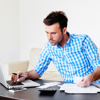 A man working on his laptop holding a lot of paperwork