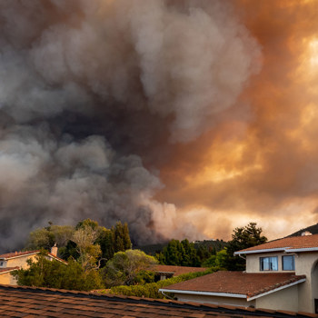 A couple houses close to a giant fire with a lot of smoke