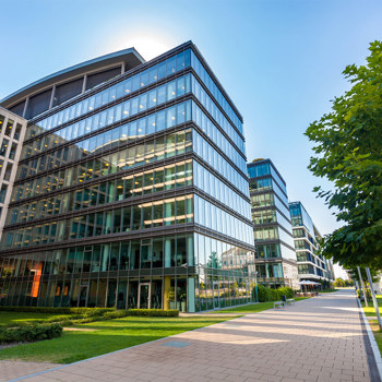 An impressive backlit glass office building with greenery.