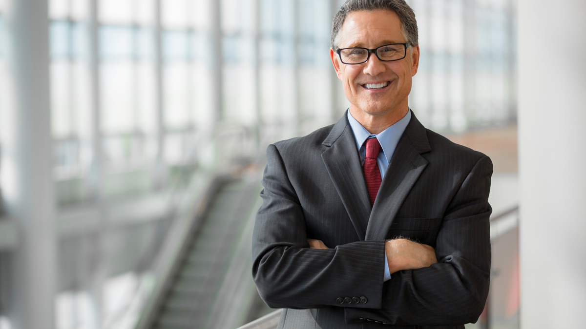 A businessman in a suit smiling in a brightly lit corridor.