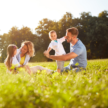 Parents playing with children outside on a sunny lawn.