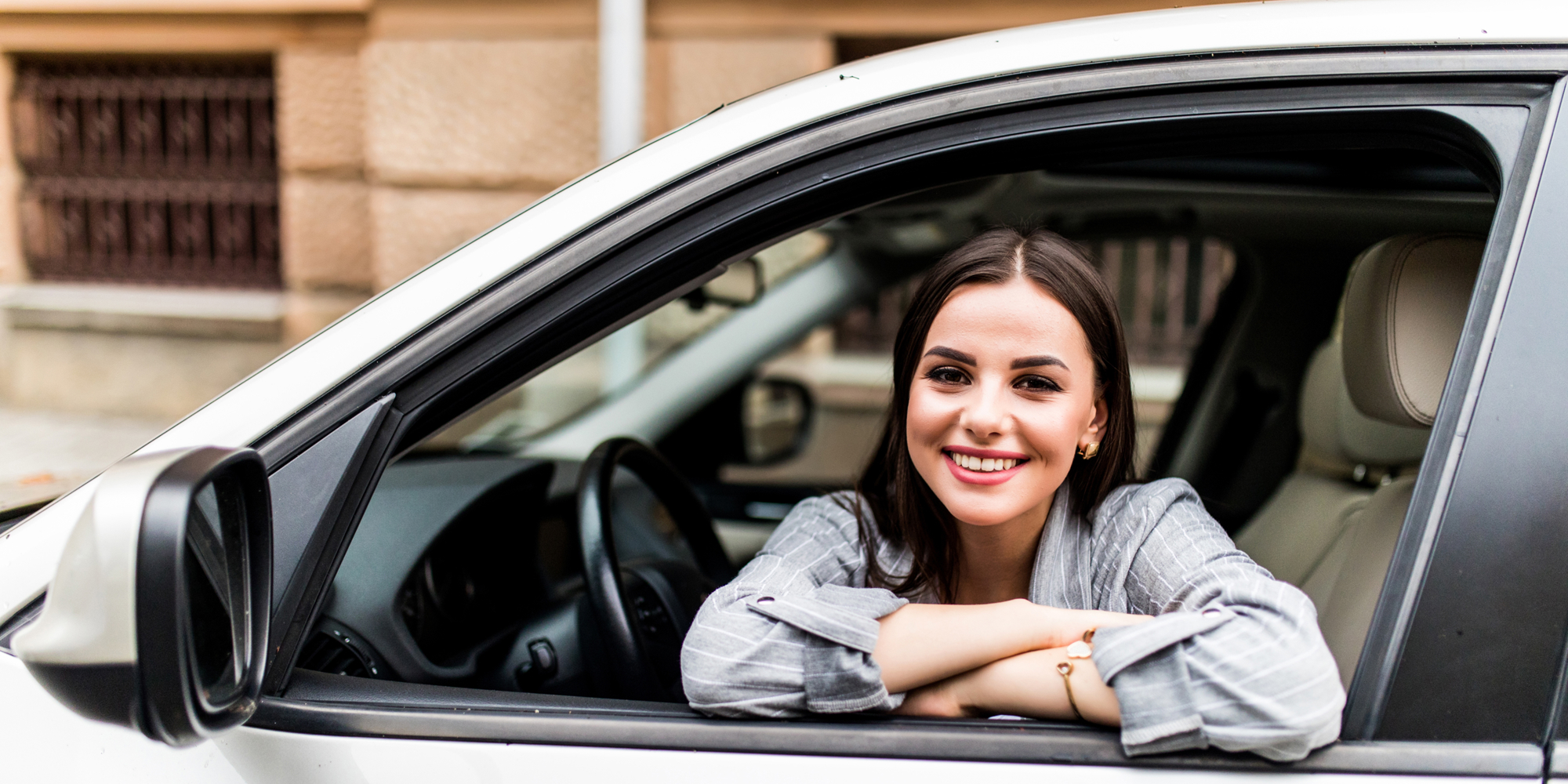 New car buyer happily sitting in the drivers seat smiling out the window
