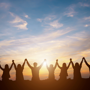A group of people putting their hands in the air during a sunset.