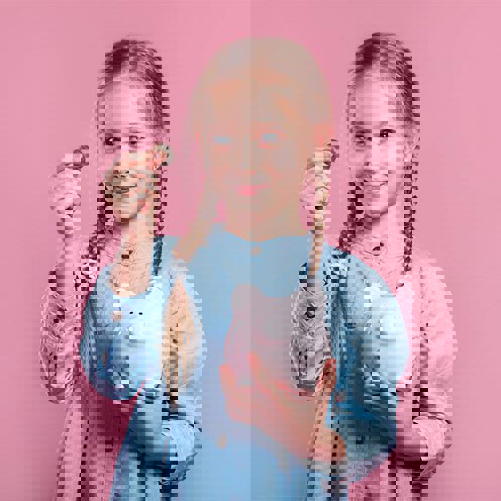 A girl holding a piggy bank and a coin in front of a pink background