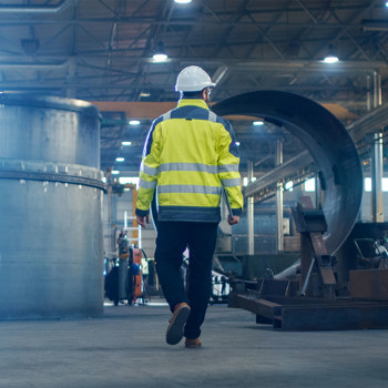 A man in a high visibility jacket inspecting large vats in a manufacturing facility.
